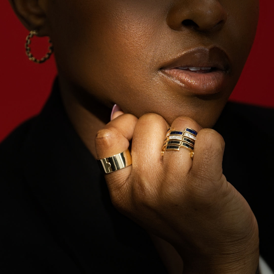 Close-up of a person wearing Bound By Love 14k gold rings with a red background Bondeye Jewelry